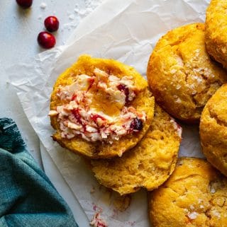Overhead close up shot of a pile of sweet potato biscuits, one with cranberry butter on it