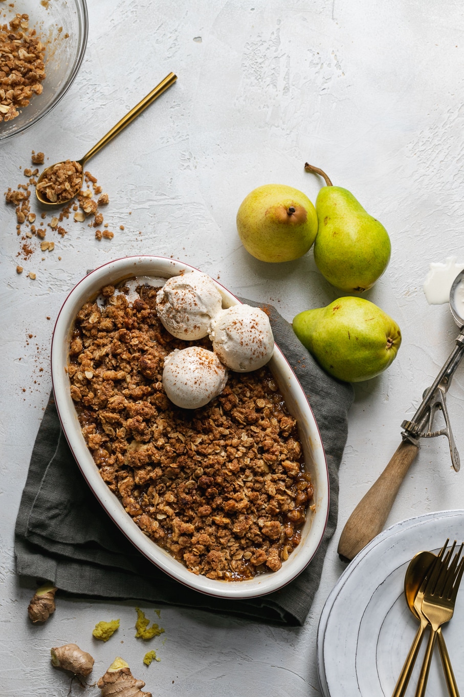 Overhead shot of a pear crisp with vanilla ice cream and a spoon digging in with pears next to it