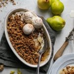 Overhead shot of a pear crisp with vanilla ice cream and a spoon digging in with pears next to it