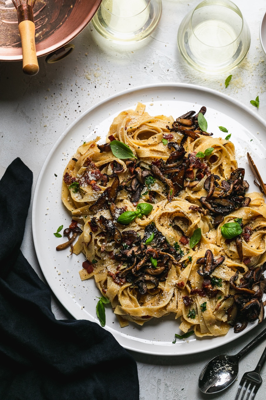 Overhead shot of pasta with mushrooms and herbs with glasses of white wine above the plate
