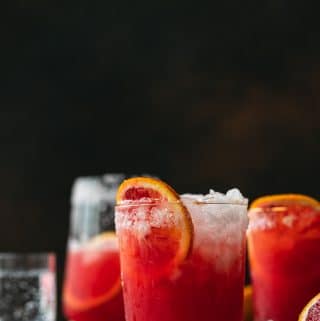 Straight on shot of blood orange paloma cocktails against a dark background