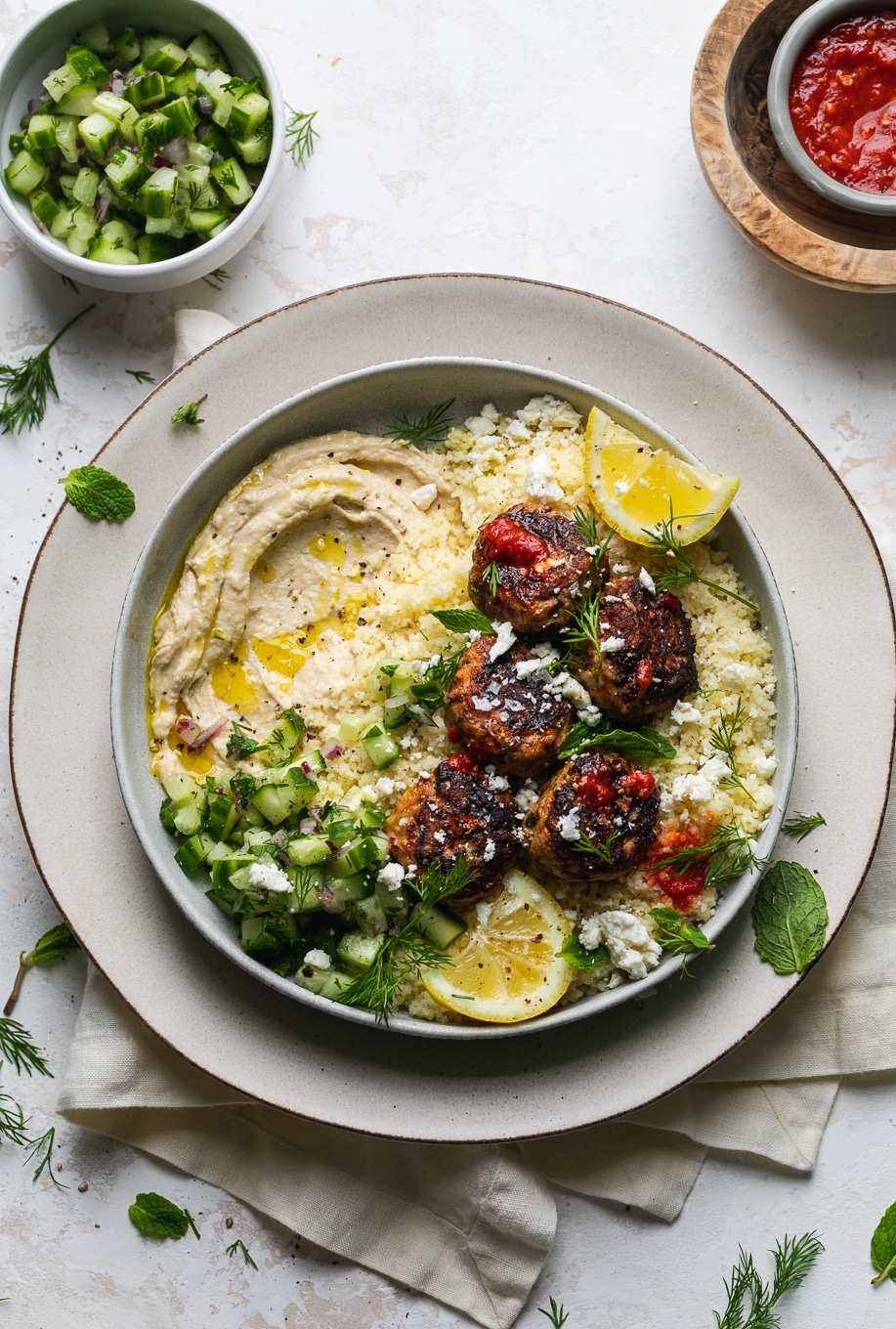 Overhead shot of a bowl with hummus, meatballs, and cucumber salad