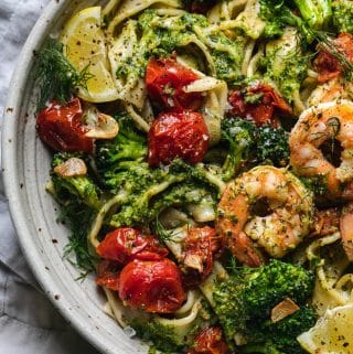 Overhead close up shot of a bowl of pasta with pesto, tomatoes, broccoli, and shrimp