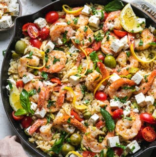 Overhead shot of a pan of orzo with shrimp, tomatoes, herbs, feta, and lemon