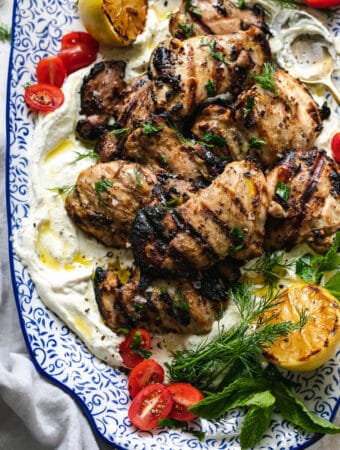 Overhead close up shot of grilled chicken thighs over whipped feta with herbs and tomatoes
