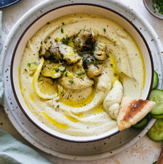 Close up shot of a bowl of hummus with pita being dipped